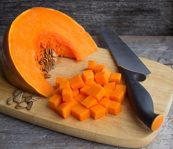 A pumpkin cut into cubes and a knife on a cutting board

Description automatically generated