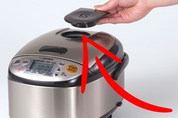 A hand holding a remote over a silver and black slow cooker
Description automatically generated