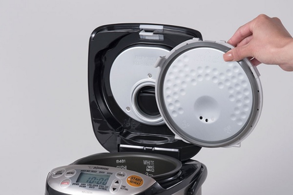 A hand holding a lid to a black and silver rice cooker
Description automatically generated