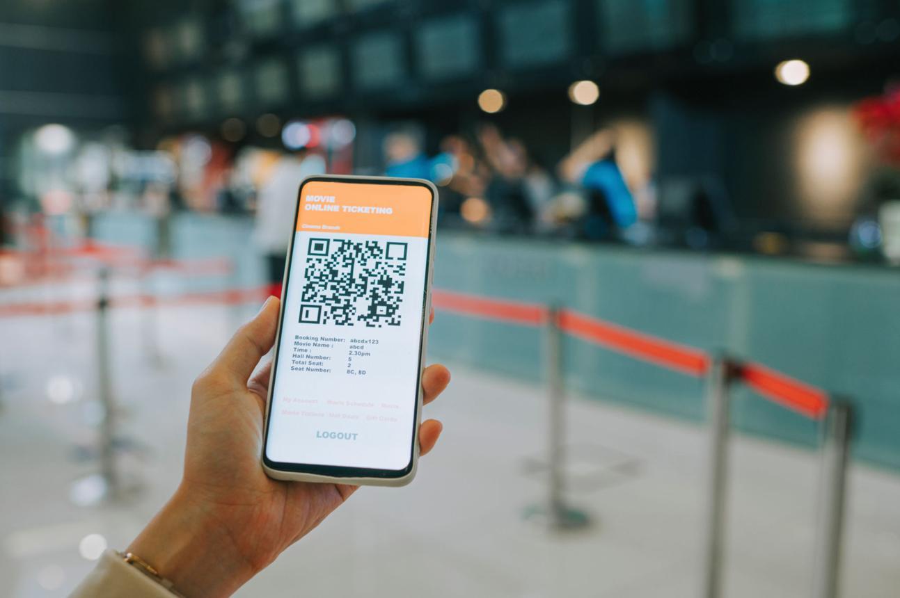 asian chinese woman using mobile app cinema movie e-ticketing reservation in front of cinema ticketing counter