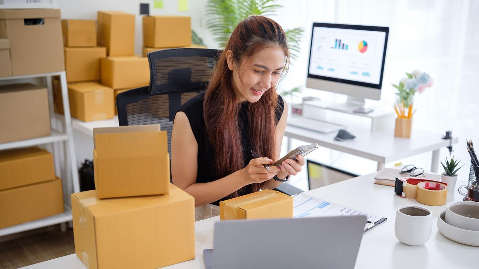Người kinh doanh sử dụng điện thoại để kiểm tra thông tin vận chuyển và tạo đơn hàng.